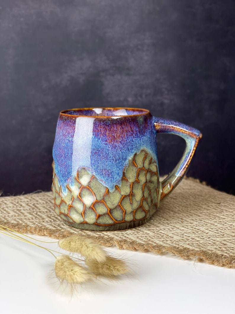 The photo shows a handmade cup with a square handle with a volume of 350 ml. It is textured and brown on the bottom, smooth and iridescent on top. This is our bestseller.