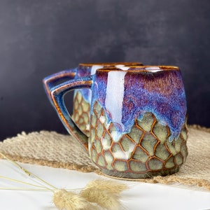 The photo shows a handmade cup with a square handle with a volume of 350 ml. It is textured and brown on the bottom, smooth and iridescent on top. This is our bestseller.