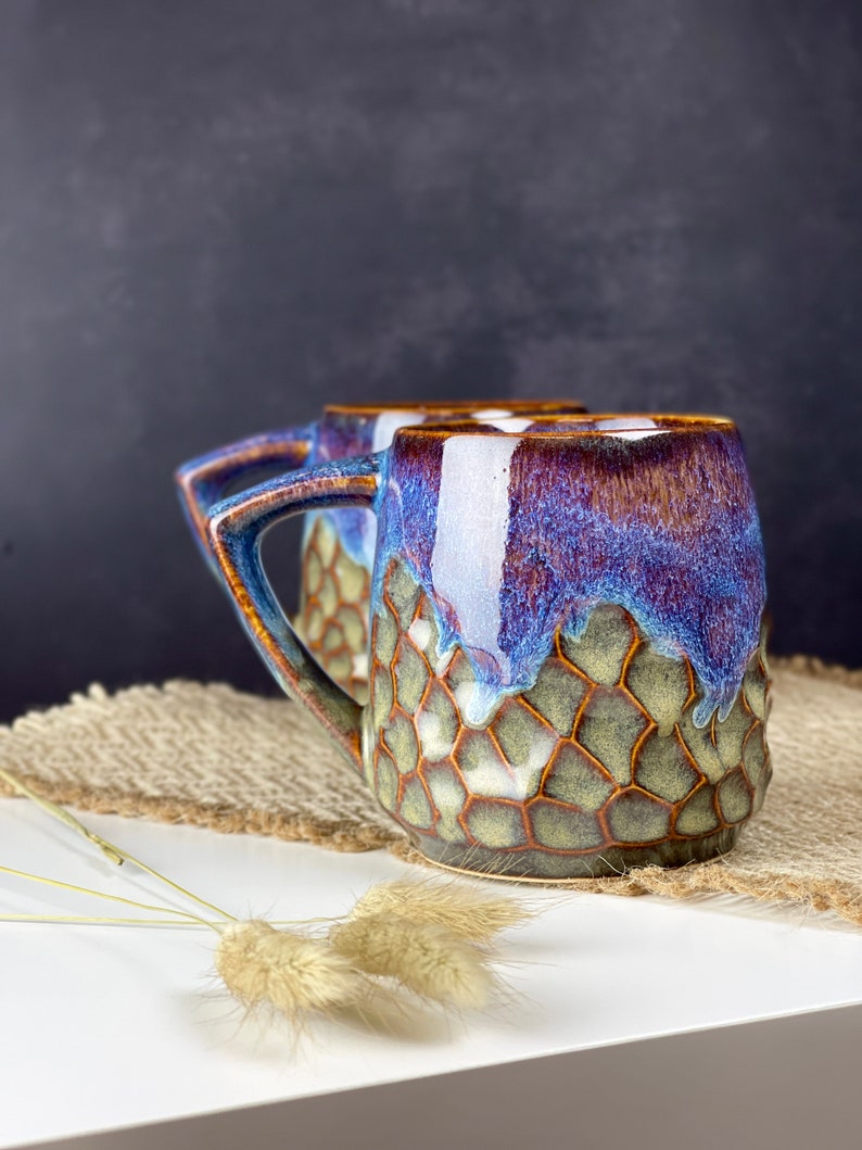 The photo shows a handmade cup with a square handle with a volume of 350 ml. It is textured and brown on the bottom, smooth and iridescent on top. This is our bestseller.