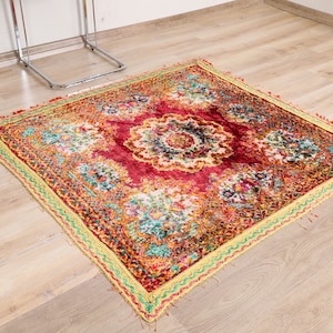 Könnte beinhalten: Ein bunter, gemusterter Teppich mit einem roten, gelben und grünen Rand. Der Teppich hat ein florales Design mit einem zentralen Medaillon.