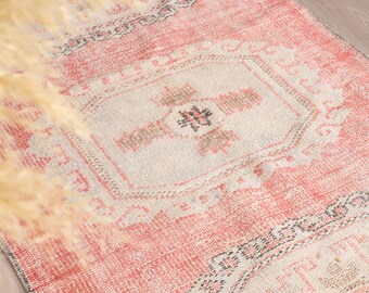 May include: A vintage-style rug with a faded pink and white colour scheme. The rug features a central diamond-shaped design with intricate floral patterns.