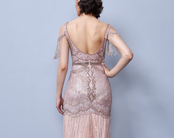 May include: A long, blush-colored sequined gown with a low back and beaded fringe detailing on the shoulders. The gown has a fitted bodice and a flowing skirt.