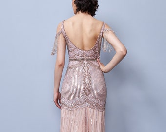 May include: A long, blush-colored sequined gown with a low back and beaded fringe detailing on the shoulders. The gown has a fitted bodice and a flowing skirt.