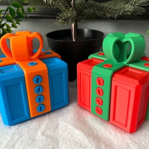 May include: Two 3D printed gift boxes, one blue with an orange bow and the other red with a green bow. Both boxes have a series of small circles on the side.