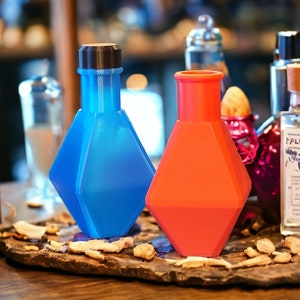 May include: Two decorative glass bottles with geometric shapes. The bottle on the left is blue and the bottle on the right is red. The bottles are sitting on a wooden surface with dried leaves.