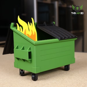 May include: A green dumpster with a black lid and a yellow and orange flame inside. The dumpster has wheels and is made of plastic. The text "THIN AIR 3D" is visible in the upper right corner of the image.