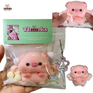 以下が含まれることがあります： ピンクの豚のキーホルダーで、羽根と星のチャームが付いています。豚は足を揃えていて、かわいい表情をしています。キーホルダーは透明なビニール袋に、ありがとうカードと一緒に梱包されています。