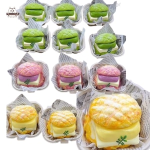 Può includere: Un assortimento di articoli colorati a forma di mini-sandwich. I panini presentano panini verdi, rosa e gialli con vari ripieni, tra cui strati bianchi e viola. Ogni sandwich è presentato in un piccolo contenitore bianco foderato con carta di giornale.