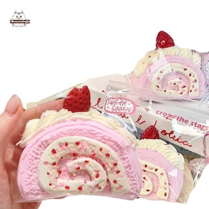 May include: A pink and white cake roll, topped with a strawberry. The cake has a cream filling and red sprinkles. The packaging includes the text "Sugar Cookie".