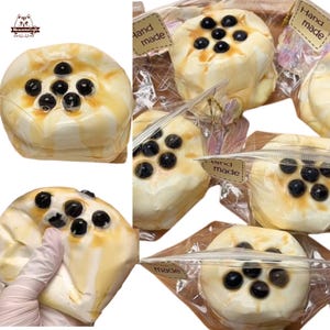 以下が含まれることがあります： 手作りの白いふわふわしたおもちゃが6個、個別に包装されています。おもちゃはケーキの形をしていて、黒いタピオカの真珠が載っています。各パッケージには「Hand Made」と書かれたラベルが付いています。