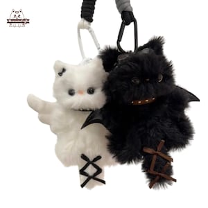以下が含まれることがあります： 天使の羽を持つ白い猫と黒いコウモリの2つのぬいぐるみキーホルダー。白い猫はリボンとクロスステッチのディテールがあります。黒いコウモリはコウモリの羽と縫い付けられた口を持っています。どちらにもキーリングが付いています。