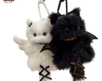 May include: Two plush keychains: a white cat with angel wings and a black bat. The white cat has a bow and cross-stitch details. The black bat has bat wings and a stitched mouth. Both have key rings attached.