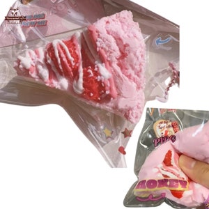 以下が含まれることがあります： 透明なプラスチック袋に入ったピンクと白のイチゴショートケーキのスクイーズおもちゃ。おもちゃは、白いフロスティングと赤いイチゴをトッピングしたケーキの切り身の形をしています。袋にはピンクと白の星柄がプリントされています。