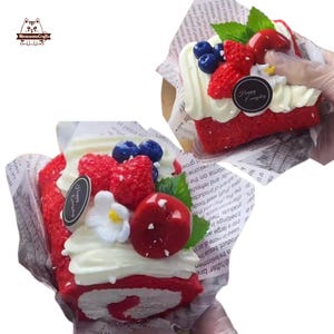 Può includere: Due fette di torta velluto rosso con glassa bianca, guarnite con frutti di bosco freschi e foglie di menta. Una fetta è avvolta in carta di giornale. Un adesivo recita "Happy Everyday". Le torte sono di MeowsomeCrafts.