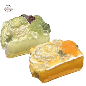 May include: Two miniature cakes with white frosting and fruit toppings. The cake on the left has green fruit and a lime slice. The cake on the right has orange slices and a green leaf.