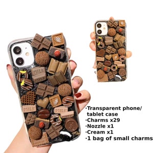 May include: A clear phone case decorated with chocolate-themed charms, including chocolate bars, candies, and sprinkles. The case is filled with a variety of brown and black charms, including chocolate bars, candies, and sprinkles. The case is made of clear plastic and has a black background.
