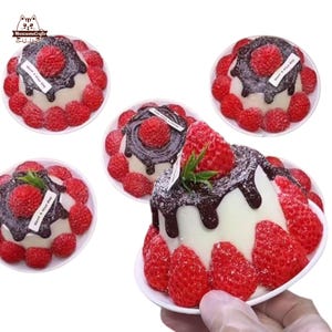 May include: Several miniature cakes with white frosting, chocolate drizzle, and fresh strawberries. Each cake is on a small white plate and has a strawberry on top. The cakes have a small white label that says "have a nice day".