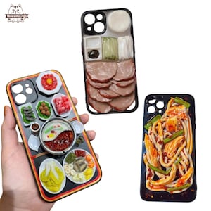 以下が含まれることがあります： 食べ物をテーマにしたデザインの携帯電話ケースが3つ。1つのケースは中華鍋のデザイン、もう1つはスライスした肉、3つ目は麺です。ケースは黒で、食べ物の詳細なレプリカが施されています。