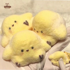 May include: Three handmade yellow plush toys shaped like a cartoon dog with black eyes and heart-shaped markings. The toys are soft and fluffy, with a light yellow color. The toys are arranged together, with one in the foreground and two in the background.