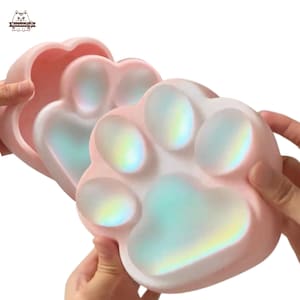 May include: A pink silicone pet food bowl shaped like a paw print. The bowl has a iridescent finish and is divided into four sections.