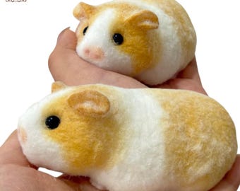 May include: Two needle felted guinea pigs, one white and brown, the other mostly white with brown accents. The guinea pigs are sitting in the palms of a person's hands.