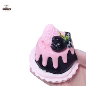 May include: A miniature cake with pink frosting dripping over a dark brown base. The cake is topped with a pink strawberry and a dark berry. The words "Happy Everyday" are on a small black rectangle.
