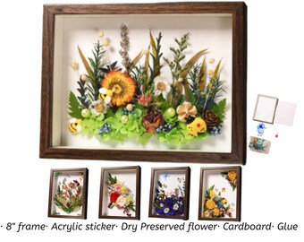 May include: A framed artwork with dried flowers, including an orange gerbera daisy, green foliage, and bee and ladybug embellishments. The frame is approximately 20 cm. Additional framed floral art pieces are displayed below.
