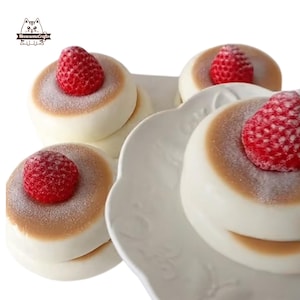 May include: Four white and brown mini cakes with a red strawberry on top of each cake. The cakes are on a white plate with a decorative edge.