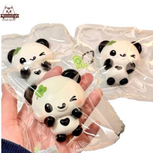 May include: Three panda-shaped charms with black and white details, each in a clear plastic bag. The pandas have black ears, eyes, and paws, with a green four-leaf clover on their heads. One panda is winking.