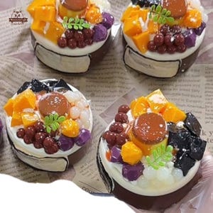 May include: Close-up of four miniature desserts with a variety of colorful toppings. Each dessert features a white base, topped with mango chunks, grapes, purple taro, and a brown custard. The desserts are arranged on a newspaper background.