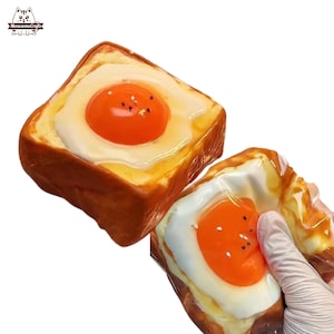 Può includere: Due fette di pane tostato con uova fritte. Il pane tostato è dorato e le uova hanno tuorli arancioni brillanti e albumi bianchi. L'immagine è un primo piano del cibo.