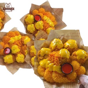 Pode incluir: Vista aérea de vários arranjos de comida. Cada arranjo apresenta comida frita marrom dourada, coberta com molho amarelo e uma pequena xícara de molho vermelho. A comida é apresentada em papel pardo com texto impresso.
