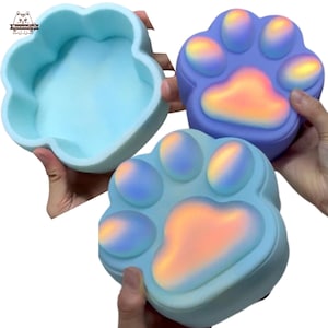 May include: Two silicone molds for making resin crafts. One mold is shaped like a paw print and the other is shaped like a flower. Both molds are light blue and have a iridescent finish.