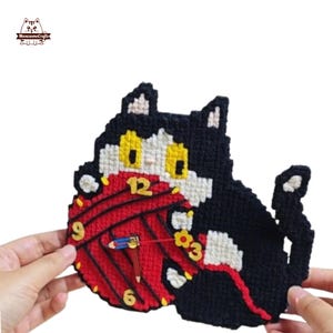 Può includere: Un orologio fatto a mano a forma di gatto con un design a palla di filo rosso. L'orologio presenta un gatto nero con occhi gialli e un muso bianco. Le lancette dell'orologio sono blu e rosse. Il quadrante dell'orologio ha i numeri 12, 3, 6 e 9 in oro.