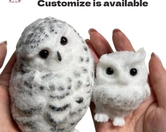 May include: Two white and gray felt owl figurines. The larger owl is sitting upright with its wings folded. The smaller owl is standing with its wings out. Both owls have black eyes.