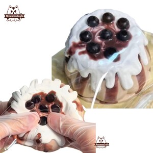 May include: A close-up of a brown and white cake with a white frosting and chocolate sauce. The cake is topped with black boba pearls. The cake is being squeezed by gloved hands.