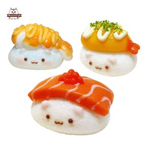 Può includere: Tre rotolini di sushi in miniatura con facce carine. I rotolini di sushi sono fatti di pasta di zucchero bianca e ricoperti con gamberi, salmone e granchio finto. I gamberi e il granchio sono decorati con pasta di zucchero gialla e arancione. Il salmone è decorato con pasta di zucchero rossa. I rotolini di sushi sono un modo divertente e fantasioso per decorare una torta o un altro dessert.