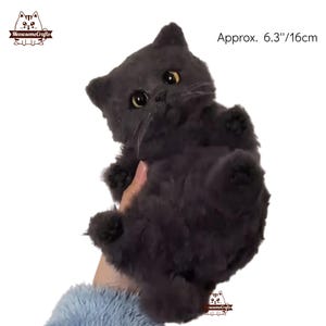 May include: A gray plush cat toy, approximately 6.3 inches or 16 centimeters tall. The cat is lying on its back with its paws in the air.