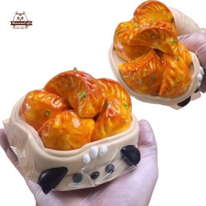 Può includere: Due contenitori di ravioli arancioni con dettagli verdi. I ravioli sono in un contenitore beige con dettagli bianchi e neri. I contenitori sono tenuti da una persona che indossa guanti. Il logo "MeowesomeCrafts" si trova in alto a sinistra.