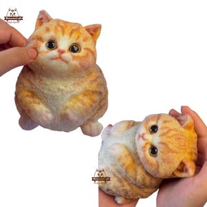 Puede incluir: Dos figuritas de gato atigrado naranja y blanco, una sentada y otra tumbada. Ambas tienen rasgos realistas y están hechas de un material suave y peludo.