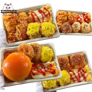 May include: Several trays of assorted food items, including fried and breaded pieces, yellow-sauced squares, and a large orange fruit. Some items are drizzled with red sauce. The trays are in a white container.