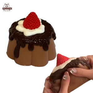 May include: A chocolate pudding dessert with a chocolate topping and a red strawberry on top. The pudding is shaped like a flower and is made of a soft, squishy material.