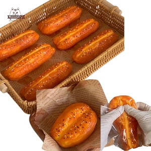 Può includere: Sei panini arancioni e marroni con semi di sesamo in un cestino di vimini. Un solo panino è mostrato in un sacchetto di plastica.