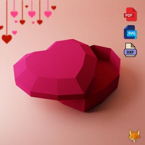 Puede incluir: Una caja de papel en forma de corazón rosa con la tapa abierta. La caja está hecha de papel doblado y tiene un diseño geométrico. La caja está sobre un fondo rosa.