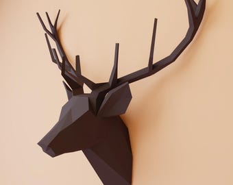 May include: A black papercraft deer head with large antlers mounted on a light brown wall.