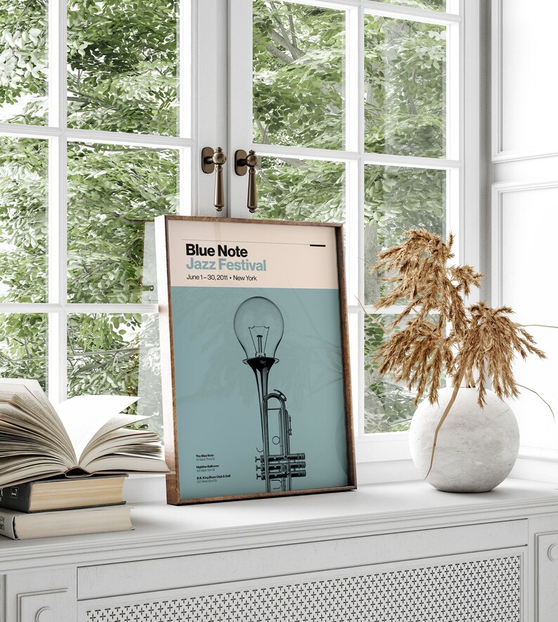 May include: A framed poster with a blue and white color scheme. The poster features a trumpet with a lightbulb on top and the text "Blue Note Jazz Festival" with the dates "June 1-30, 2021" and the location "New York".