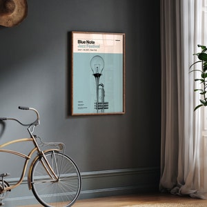May include: A poster with a light blue background featuring a black and white illustration of a trumpet with a light bulb on top. The poster has the text "Blue Note Jazz Festival" and "June 1-30, 2023 - New York" printed on it.