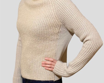May include: A beige knitted sweater with a mock neck and long sleeves. The sweater has a ribbed texture and a slightly fitted silhouette.