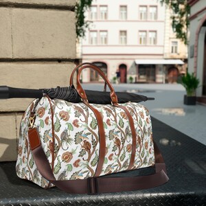May include: A white and brown travel bag with a floral and monkey pattern. The bag has a brown leather handle and a brown adjustable shoulder strap.