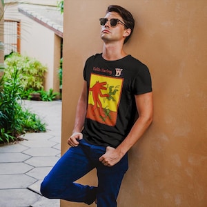 Puede incluir: Una camiseta negra con un estampado gráfico amarillo y rojo de un diseño de Keith Haring. El diseño presenta una figura roja con una figura verde saltando sobre ella. El texto "Keith Haring" está impreso sobre el diseño.